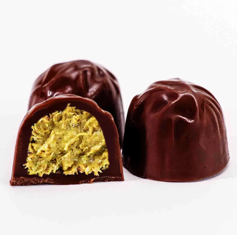 Chocolate truffles with one cut open to reveal a Dubai Chocolate filling on a white background